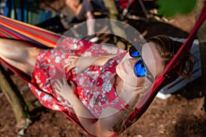 Portrait of young beautiful blonde cheerful girl enjoy in hammock outdoor. Relaxing in the hammock in the summer garden