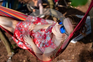 Portrait of young beautiful blonde cheerful girl enjoy in hammock outdoor. Relaxing in the hammock in the summer garden