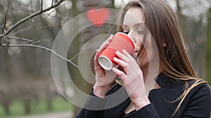 Portrait of young beautiful blonde hipster woman posing on the autumn park background and drinking cup of takeaway