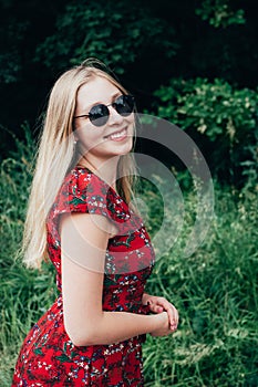 Portrait of young beautiful blonde long haired smiling teenage girl in sunglasses wearing red dress. Vertical image