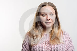 Portrait of a young beautiful blonde woman with absolutely not make up in pink knitted sweater against white background