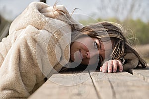 Portrait of young, beautiful, blonde woman with coat, sitting on a wooden bench with her head resting on the table, with serious