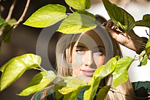 Portrait of young, beautiful, blonde woman with green eyes, looking through the green leaves of a plant. Concept beauty, eyes,