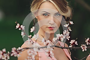 Portrait of young beautiful blonde woman in pink dress near blooming tree with white flowers on a sunny day. Spring, girl near a