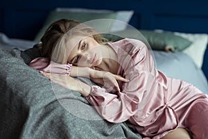 Portrait of a young beautiful blonde woman with wavy hair in a pink peignoir with a deep cut