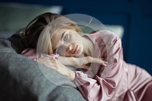 Portrait of a young beautiful blonde woman with wavy hair in a pink peignoir with a deep cut