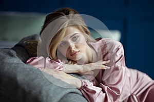 Portrait of a young beautiful blonde woman with wavy hair in a pink peignoir with a deep cut