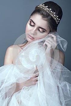 Portrait of young beautiful bride in diadem with naked shoulders touching fluffy skirt of her wedding dress with her cheek