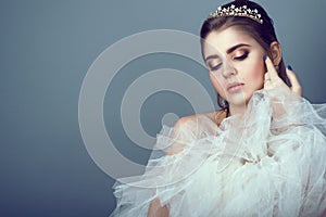 Portrait of young beautiful bride in diadem pressing fluffy skirt of her wedding dress to her breast