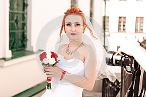 Portrait of a young beautiful bride in red sneakers with bouquet of roses on the city street.