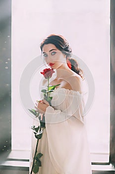Portrait young bride woman. White medieval luxury sexy dress. Red rose in hands.