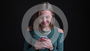 Portrait of young and beautiful brunette caucasian girl laughing watching into smartphone on black background.