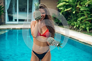 Portrait of young beautiful brunette girl in swimsuit with pineapple in her hands fruit holding on the breast.