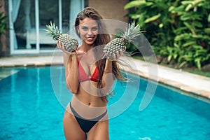 Portrait of young beautiful brunette girl in swimsuit with pineapple in her hands fruit holding on the breast.