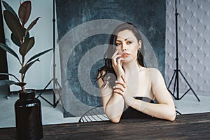 Portrait of young beautiful brunette woman sitting at table on dark gray copy space background. Gorgeous natural beauty girl in