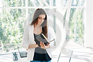 Portrait of young beautiful business woman reading notebook in modern creative office