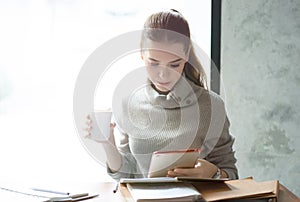 Portrait of a young beautiful businesswomen enjoying coffee during work on digital tablet while sitting in modern office.