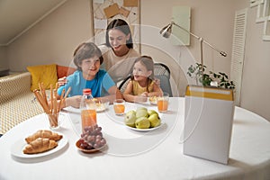 Portrait of young beautiful caucasian family, mother and her two cute little kids sitting at the kitchen table at home