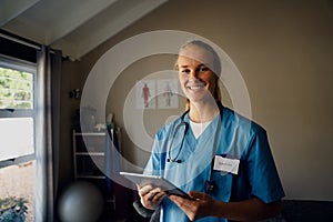 Portrait of young beautiful Caucasian female doctor in scrubs with digital tablet, smiling