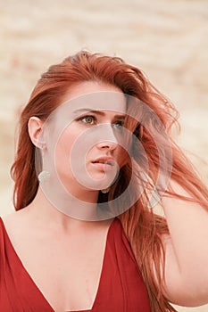 Portrait of Young beautiful Caucasian redheaded woman posing in desert landscape with sand.