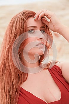 Portrait of Young beautiful Caucasian redheaded woman posing in desert landscape with sand.