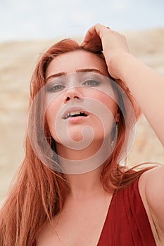 Portrait of Young beautiful Caucasian redheaded woman posing in desert landscape with sand.