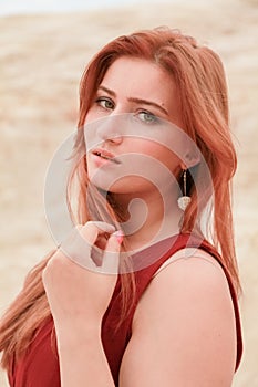 Portrait of Young beautiful Caucasian redheaded woman posing in desert landscape with sand.