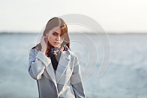 Portrait of a young beautiful charismatic brunette girl in a coat on the coast of the sea