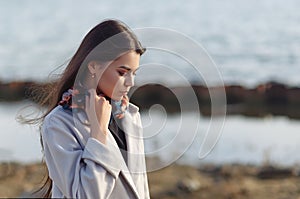 Portrait of a young beautiful charismatic brunette girl in a coat on the coast of the sea