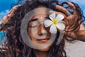 Portrait of young and beautiful cheerful woman with frangipani flower on the beach