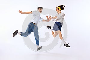 Portrait of young beautiful couple, man and woman, dancing retro dance isolated over white studio background. Cheerful