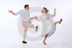 Portrait of young beautiful couple, man and woman, dancing retro dance isolated over white studio background. Enjoyment