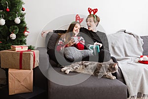 Portrait of young beautiful couple sitting on sofa at home and wearing deer horns while happily spending time together