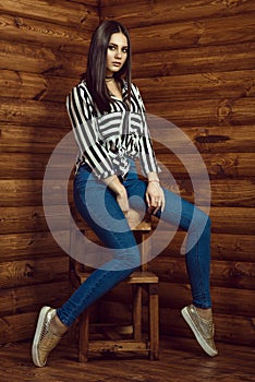 Portrait of young beautiful dark-haired model wearing skinny high-waisted jeans, striped shirt, choker and golden sneakers