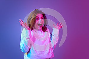 Portrait of young beautiful emotive girl smiling, laughing against gradient blue purple studio background in neon light