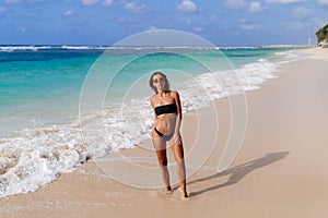 Portrait of young beautiful european woman in swimsuit and sunglasses standing on ocean beach