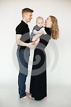 Portrait of young beautiful family in dark clothes with plump cherubic baby infant toddler standing on white background.