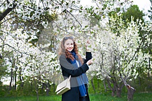 Portrait of a young beautiful fashionable woman in spring blossoming park. Happy girl posing in a blooming garden with white