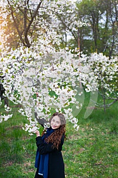 Portrait of a young beautiful fashionable woman in spring blossoming park. Happy girl posing in a blooming garden with white