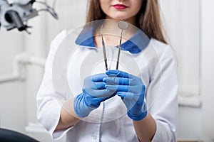 Portrait of young beautiful female dentist holding dental tools at the modern dental office