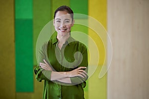 Portrait of a young beautiful female office worker keeping arms crossed, looking at camera and smiling while standing in