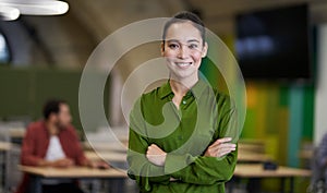 Portrait of a young beautiful female office worker keeping arms crossed, looking at camera and smiling while standing in