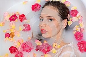 Portrait of a young beautiful girl in a bath with rose petals. Closeup