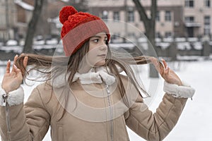 Portrait of a young beautiful girl in a beige coat and red hat on the background of a winter park