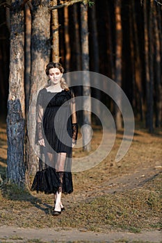 Portrait of a young beautiful girl in a black dress strolling in the park among the trees.