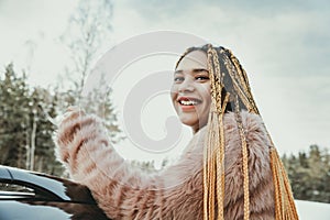 Portrait of a young beautiful girl with box braids hairstyle  next to a car in winter nature