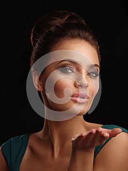 Portrait of a young beautiful girl with collected hair and expressive make up on the black background sends a kiss