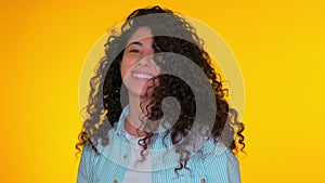 Portrait of young beautiful girl corrects her curls on yellow background. Trendy cute woman smiling to camera. Studio
