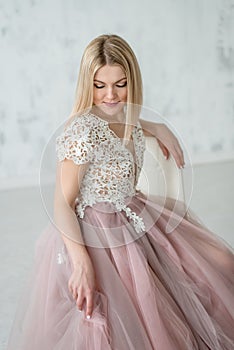 Young beautiful girl in an evening dress with lace and pink fartine on the background of a white textural wall.