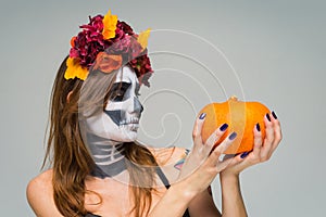 Portrait of young beautiful girl with fearful halloween skeleton makeup with a wreath Katrina Calavera made of flowers on her head